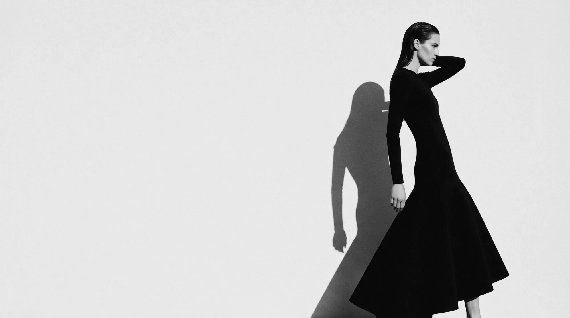 Model in a black dress, shadow cast on a pale wall